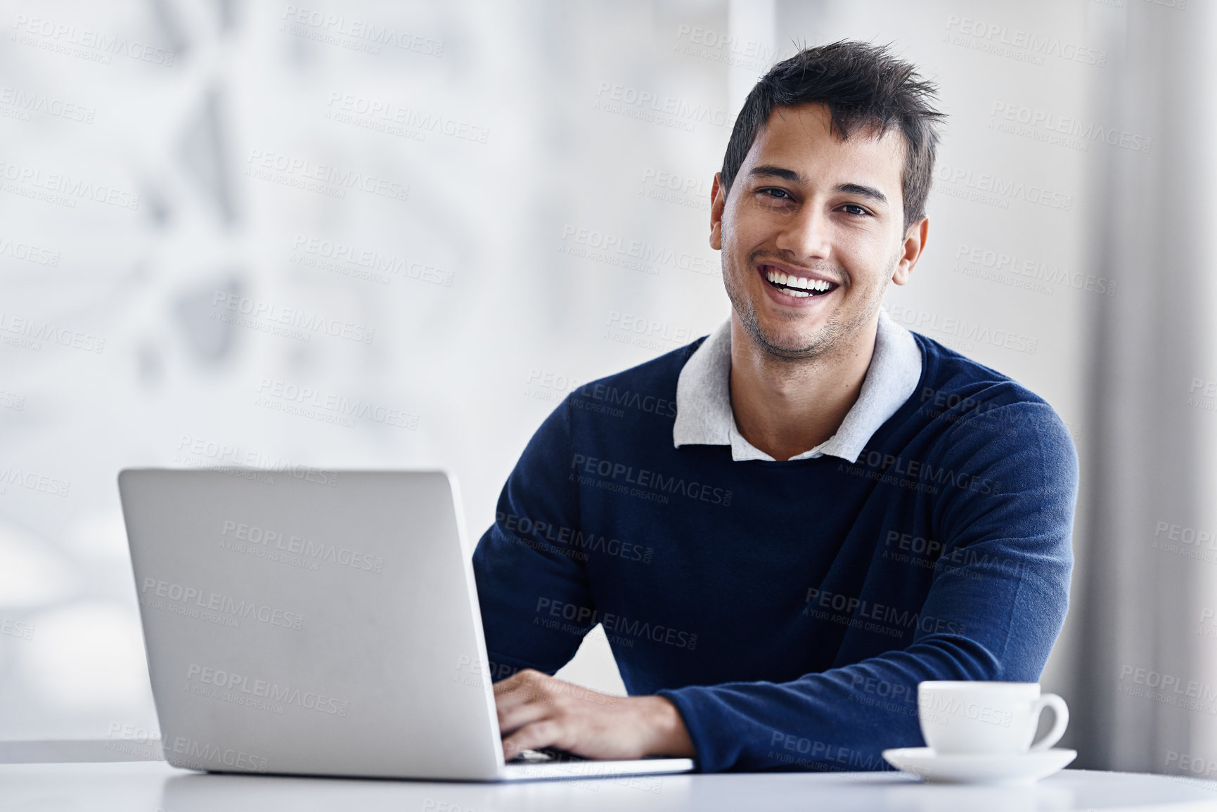 Buy stock photo Portrait of a smiling young businessman using a laptop while sitting at a desk in an office