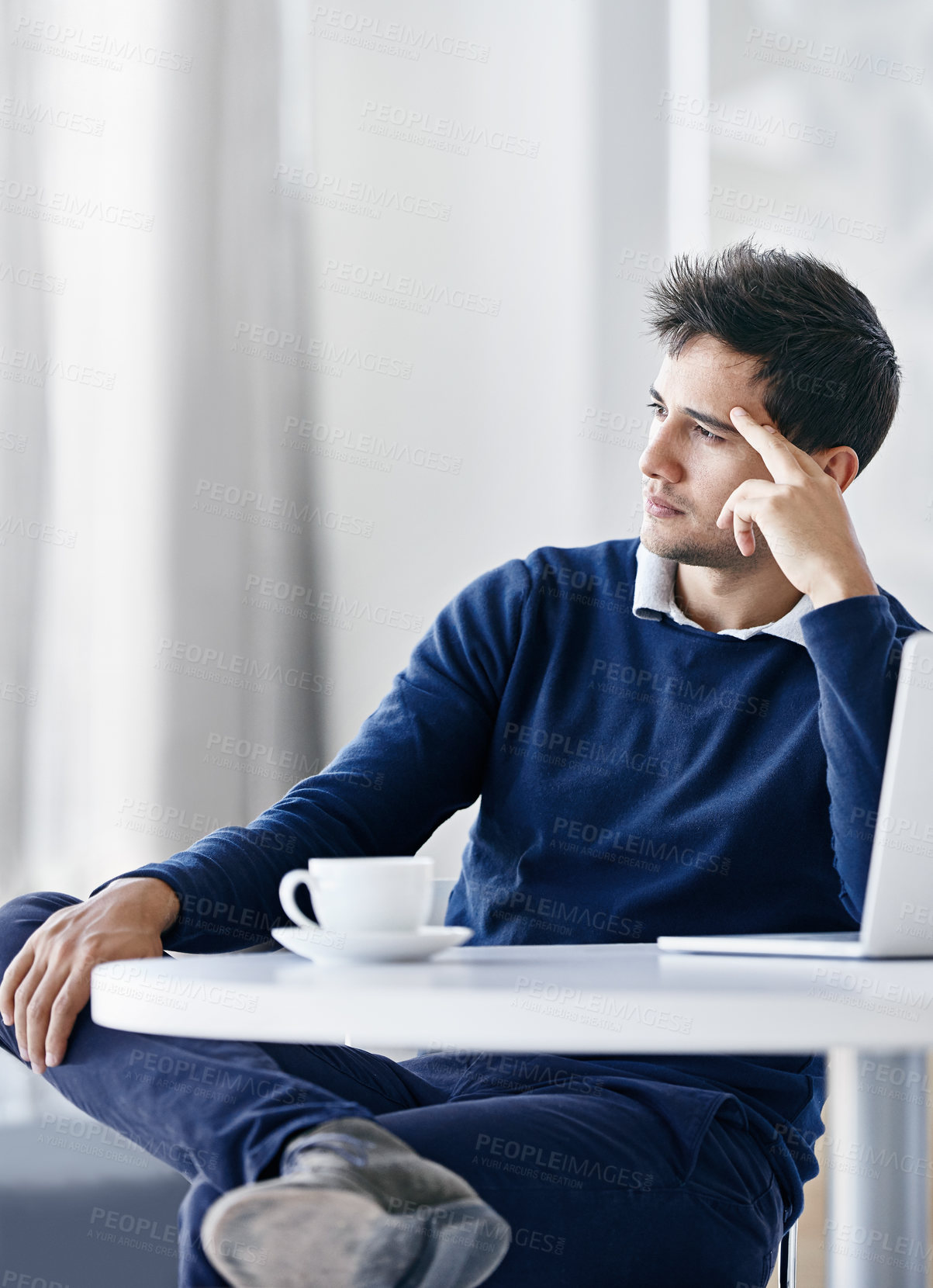 Buy stock photo Shot of a thoughtful young businessman using a laptop while sitting at a desk in an office