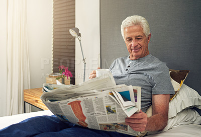 Buy stock photo Shot of a senior man reading the newspaper in bed while having coffee