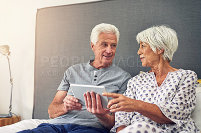 Buy stock photo Shot of a senior couple using a tablet while lying in bed