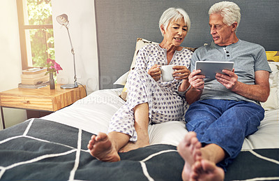 Buy stock photo Shot of a senior couple using a tablet while lying in bed
