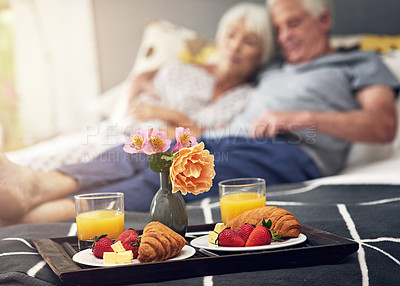Buy stock photo Shot of a tray of breakfast on a bed with a couple blurred in the background