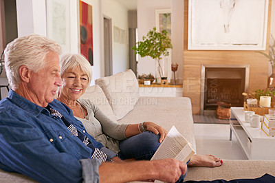 Buy stock photo Shot of a relaxed senior couple reading a book together on the sofa at home