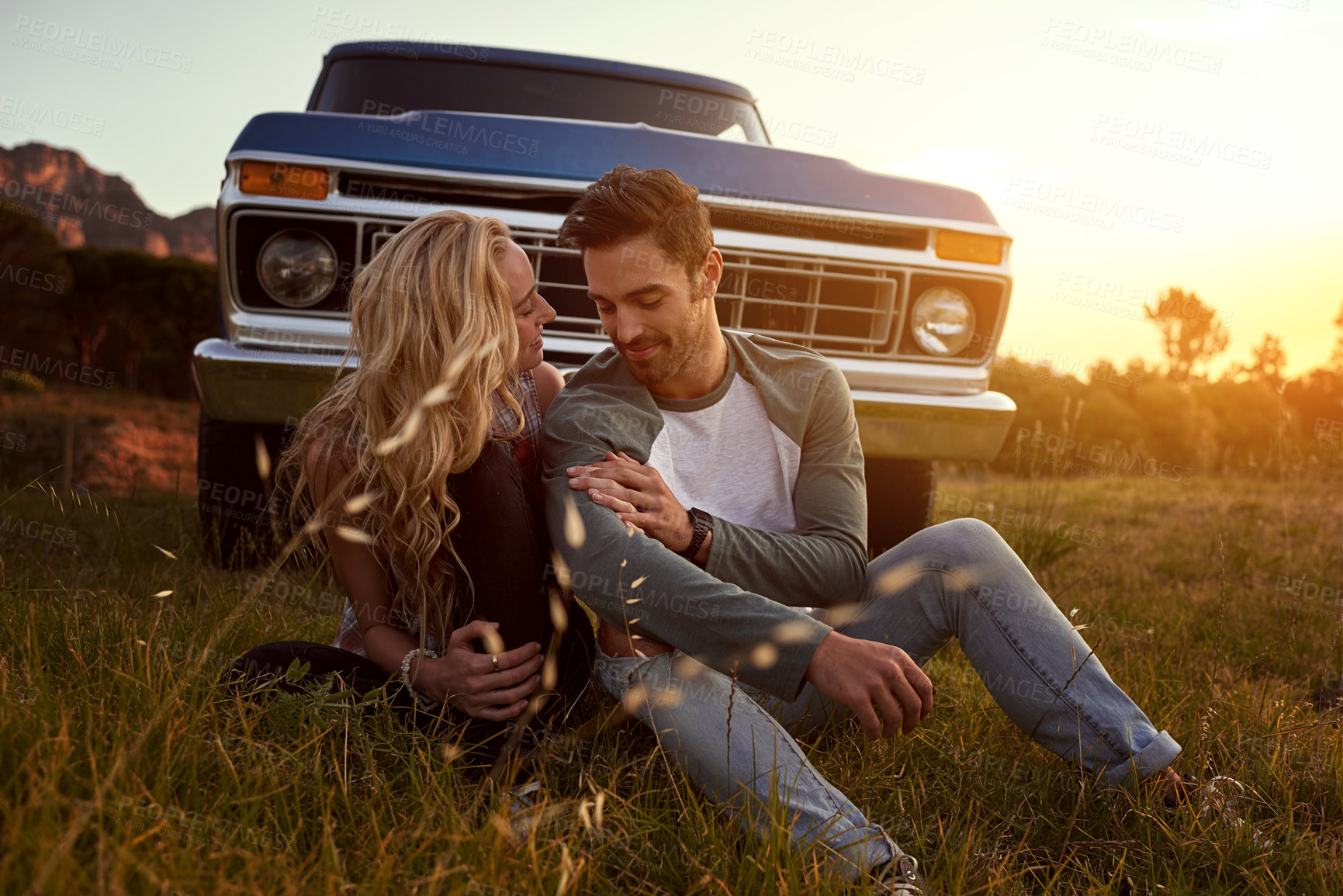 Buy stock photo Relax, outdoor and couple by car for travel by sunset on vacation, weekend or holiday. Happy, love and young man and woman in field by vehicle for road trip getaway together in evening in nature.