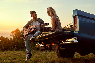 Buy stock photo Shot of a young man playing guitar for his girlfriend on a roadtrip