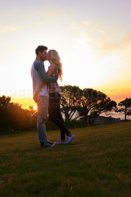 Buy stock photo Shot of an affectionate young couple sharing a kiss at sunset