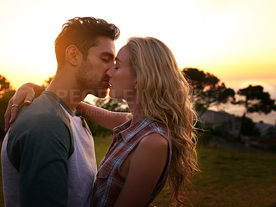 Buy stock photo Shot of an affectionate young couple sharing a kiss at sunset