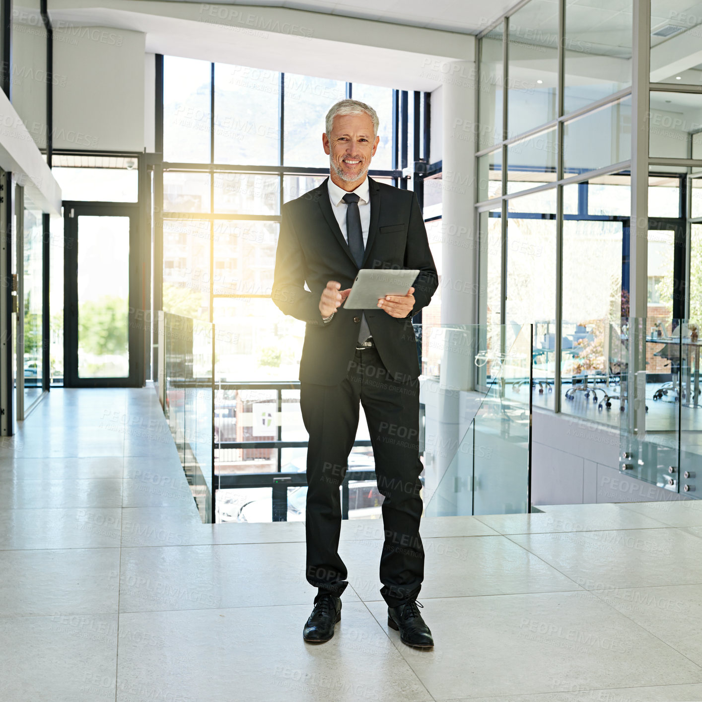 Buy stock photo Shot of a mature businessman standing in a modern office using a digital tablet