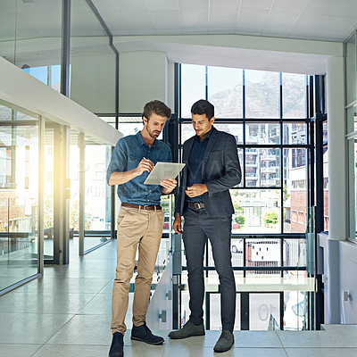 Buy stock photo Shot of two colleagues talking together over a digital tablet while standing in a modern office