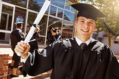 Buy stock photo Portrait of a smiling university student holding his diplomas outside on graduation day
