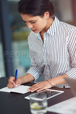 Buy stock photo Shot of a young businesswoman writing notes at an office desk