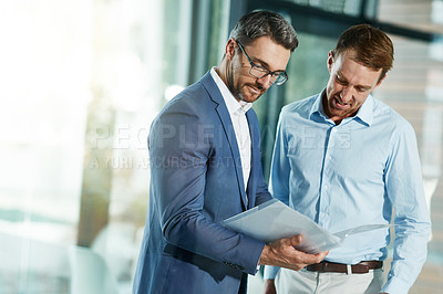 Buy stock photo Shot of two businessmen talking over some paperwork in an office