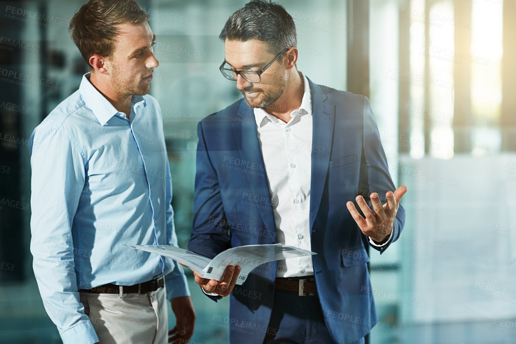 Buy stock photo Shot of two businessmen talking over some paperwork in an office