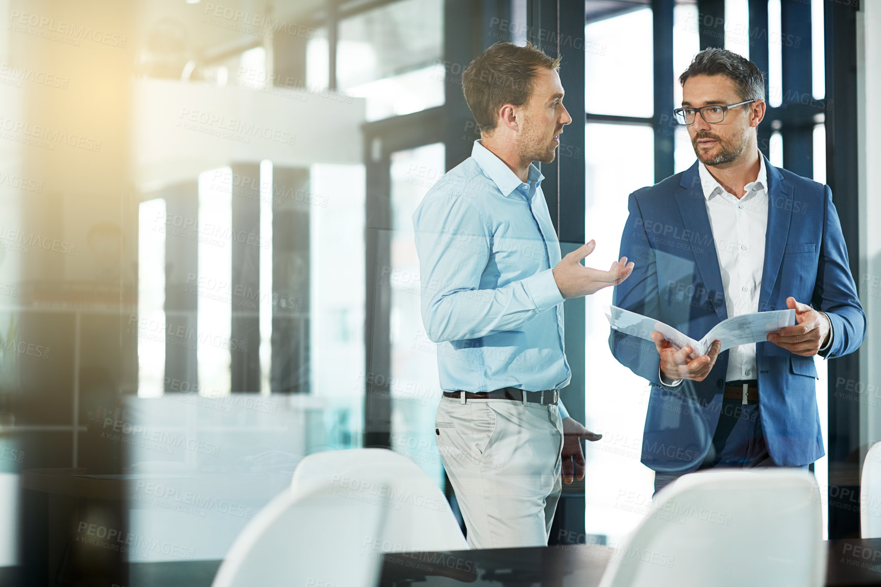 Buy stock photo Shot of two businessmen talking over some paperwork in an office