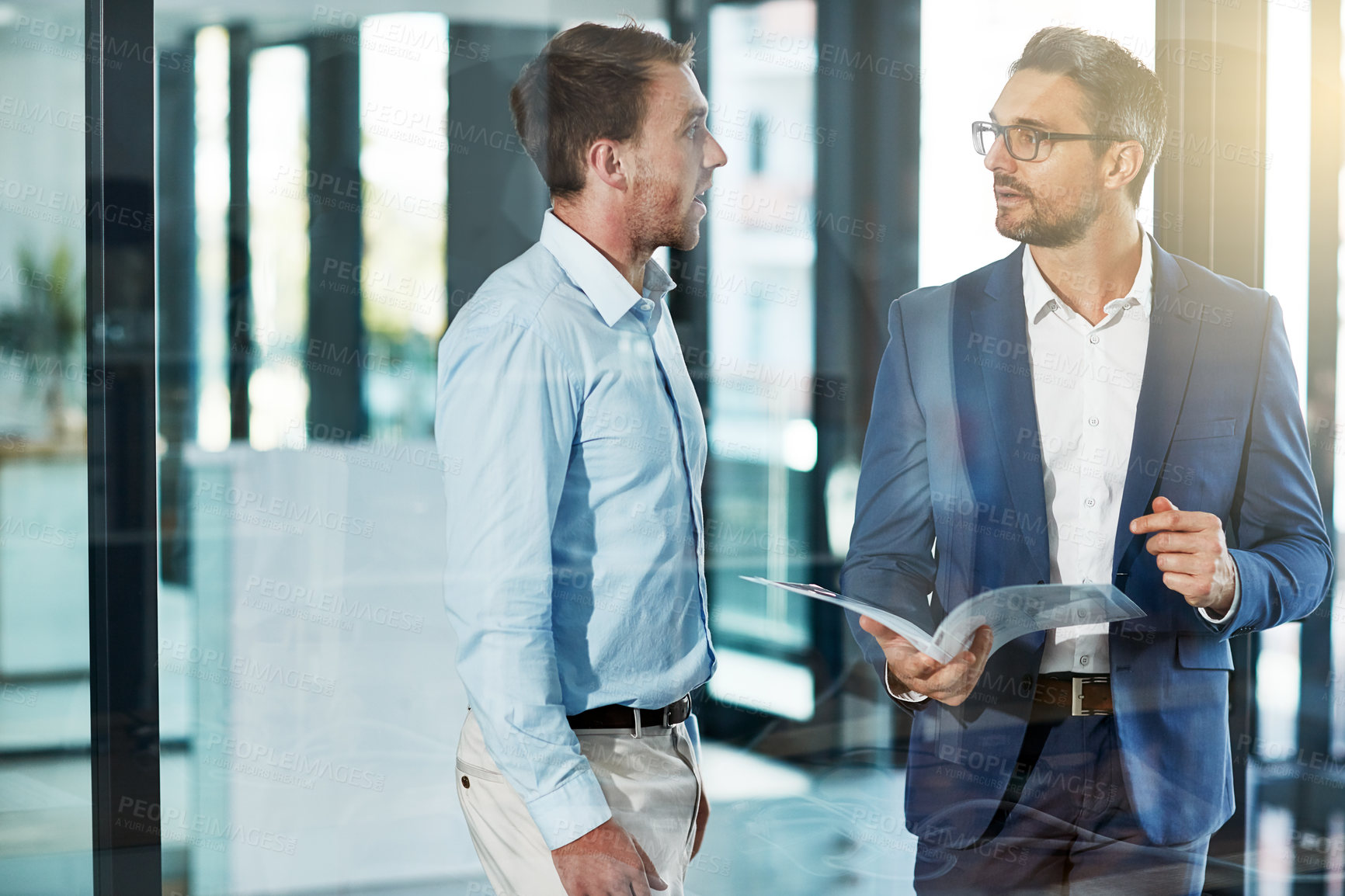 Buy stock photo Shot of two businessmen talking over some paperwork in an office