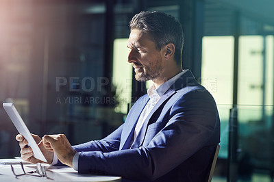 Buy stock photo Shot of a businessman using a digital tablet while woking late at the office