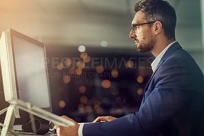 Buy stock photo Shot of a businessman using a computer while woking late at the office