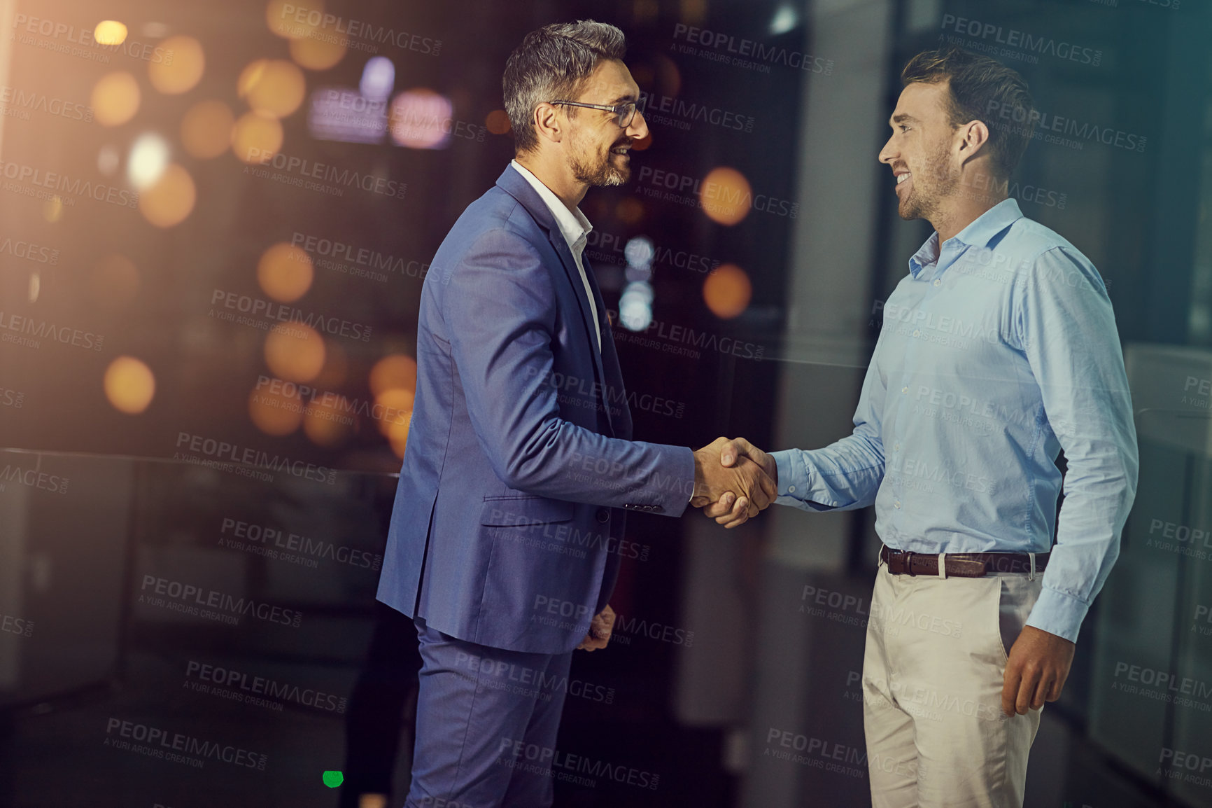 Buy stock photo Shot of two businessmen shaking hands while woking late at the office