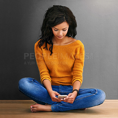 Buy stock photo Studio shot of a young woman using her phone against a gray background