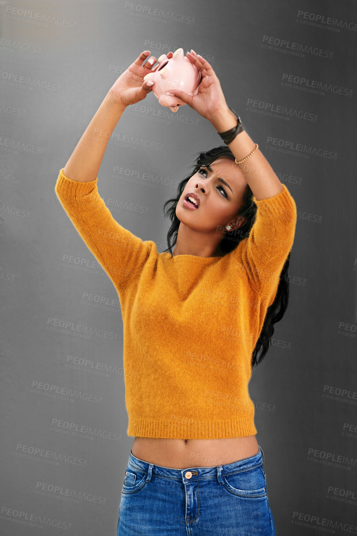 Buy stock photo Studio shot of a young woman looking up at her piggybank against a gray background