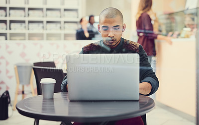Buy stock photo Shot of a young man using his laptop in a coffee shop