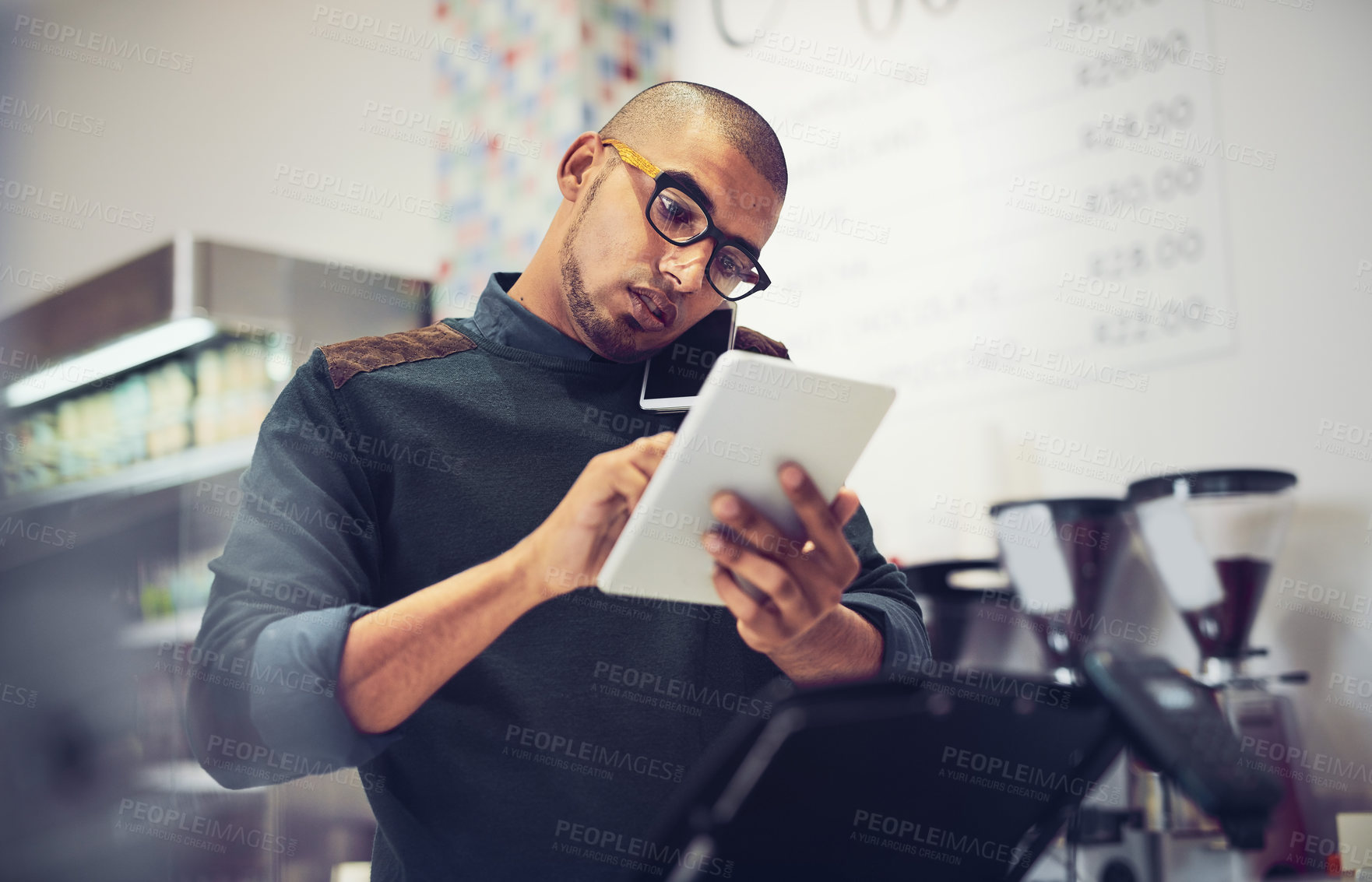 Buy stock photo Shot of a man talking on his cellphone in a coffee shop while using a digital tablet