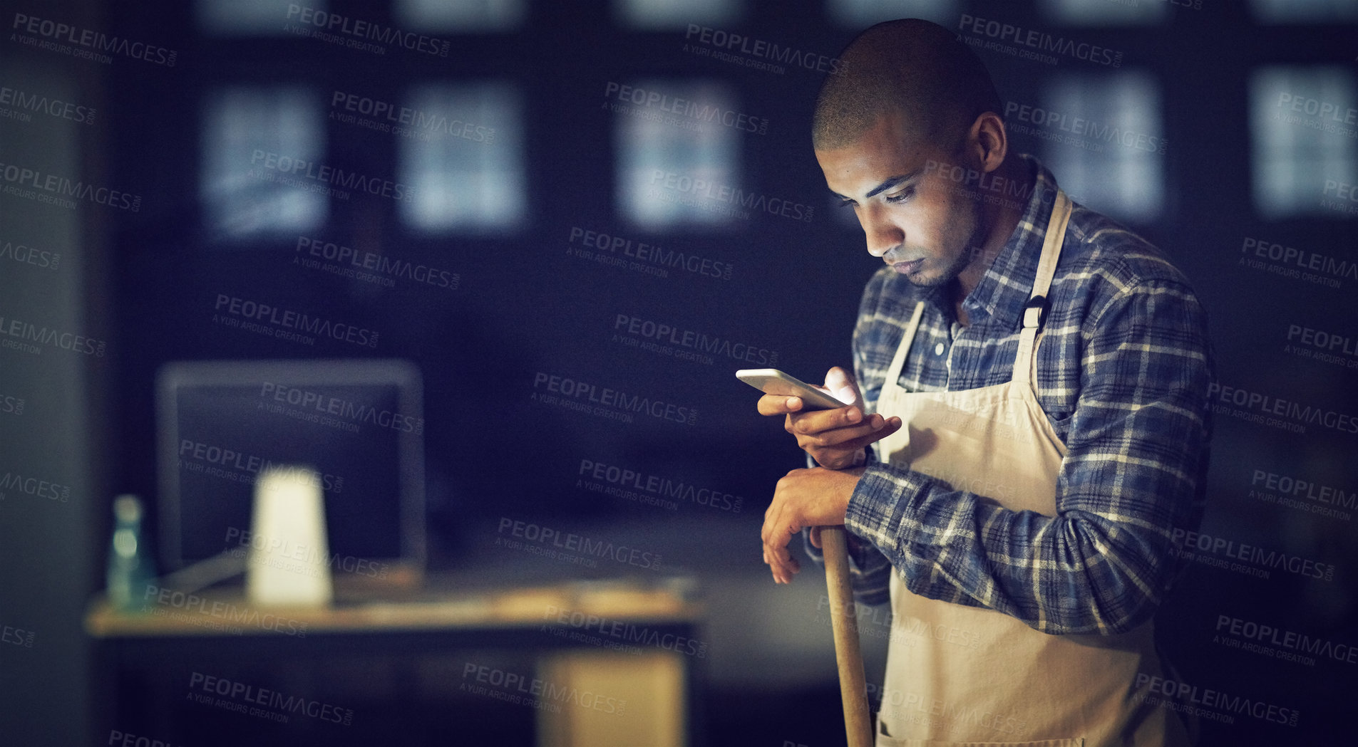 Buy stock photo Shot of a young man working late on a cellphone in his coffee shop