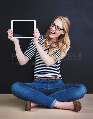 Buy stock photo Studio shot of a young woman holding a digital tablet against a dark background