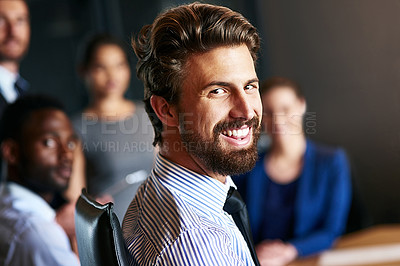 Buy stock photo Portrait of a smiling businessman sitting in an office with colleagues in the background