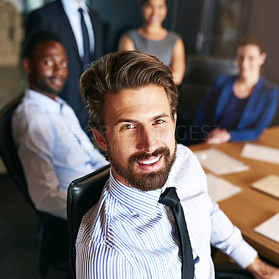 Buy stock photo Portrait of a smiling businessman sitting in an office with colleagues in the background