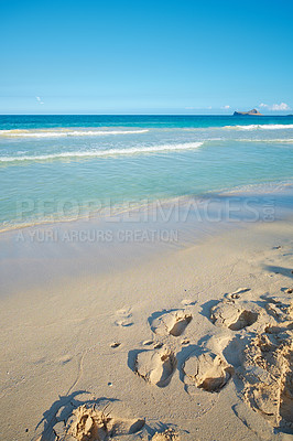 Buy stock photo Waves washing onto sandy beach shore with footprints on a tropical and exotic resort with clear blue sky background and copyspace. Relaxing summer seascape to enjoy a peaceful holiday