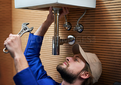 Buy stock photo Shot of a plumber repairing a pipe underneath a sink