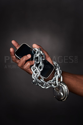 Buy stock photo Cropped shot of a man’s phone tied to his hand with chains against a black background