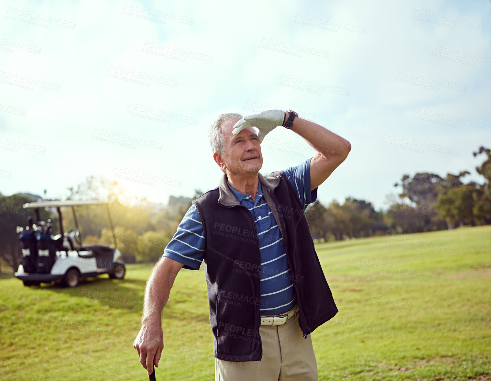 Buy stock photo Shot of a senior man shielding his eyes from the sun while playing golf