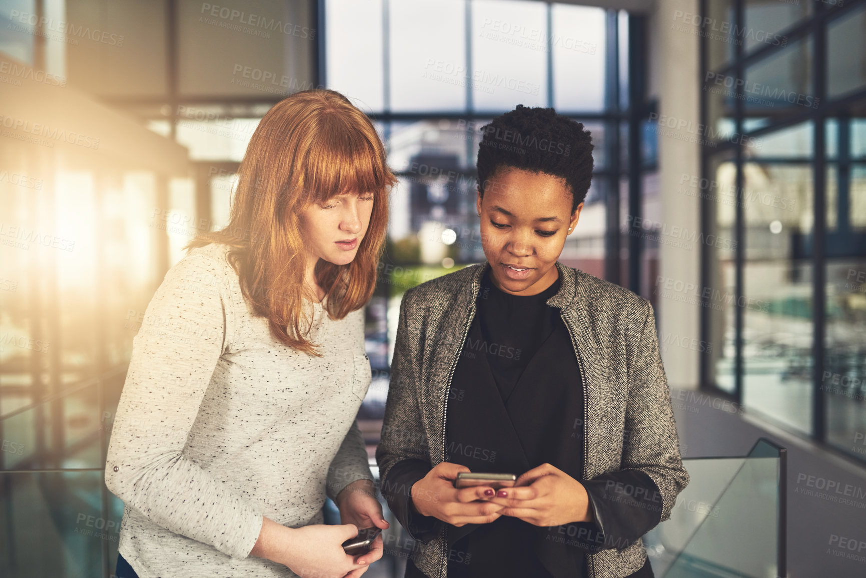 Buy stock photo Shot of two coworkers talking together over a cellphone while standing in an office