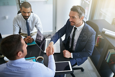Buy stock photo Cropped shot of two businessmen shaking hands while sitting in a meeting