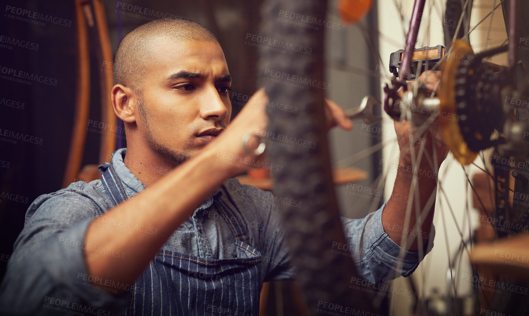 Buy stock photo Small business, man and mechanic on bicycle wheel for fixing, repairs or maintenance at workshop. Male person, employee and serious handyman at garage for service, inspection and safety as technician