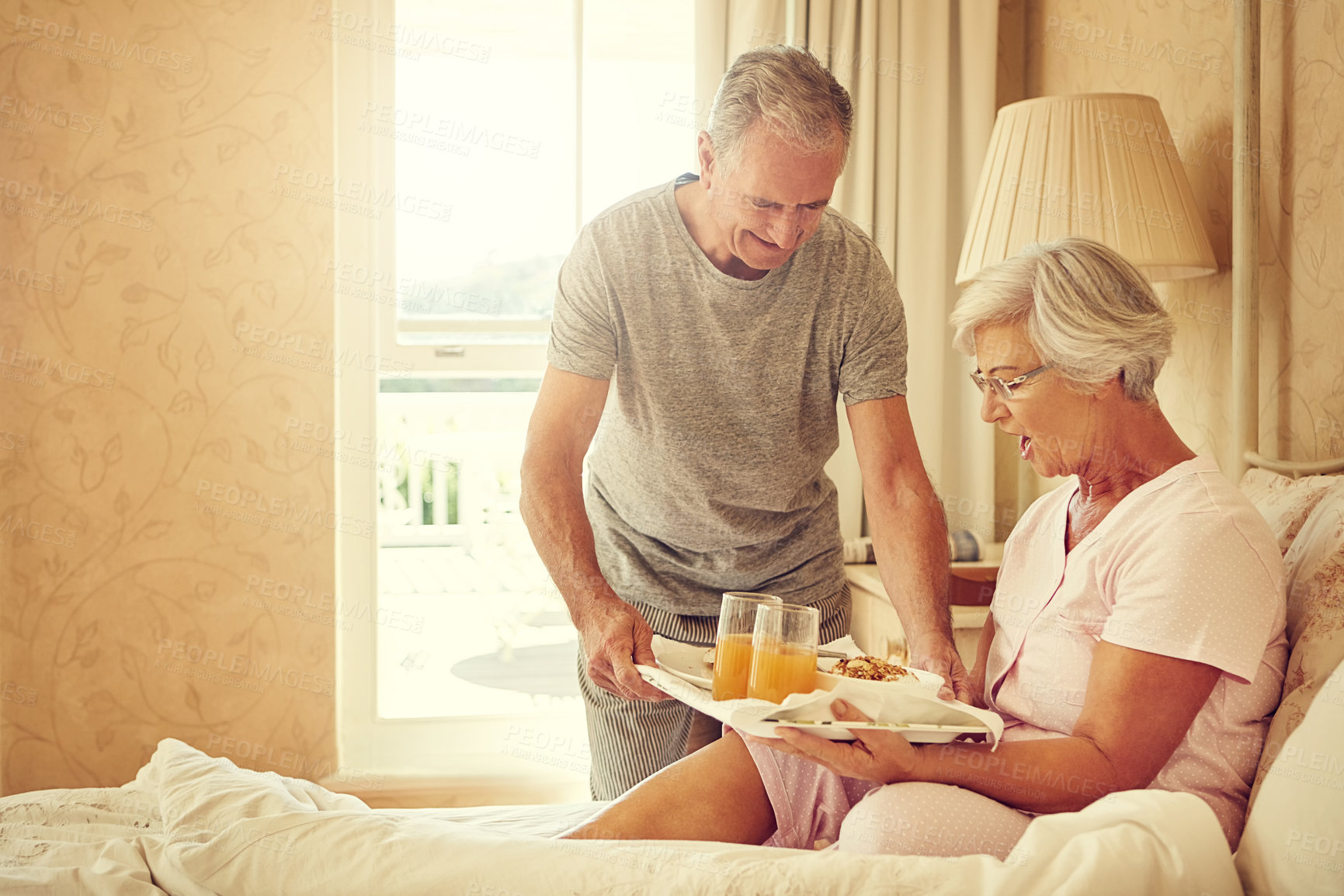 Buy stock photo Shot of a senior man bringing breakfast in bed to his wife