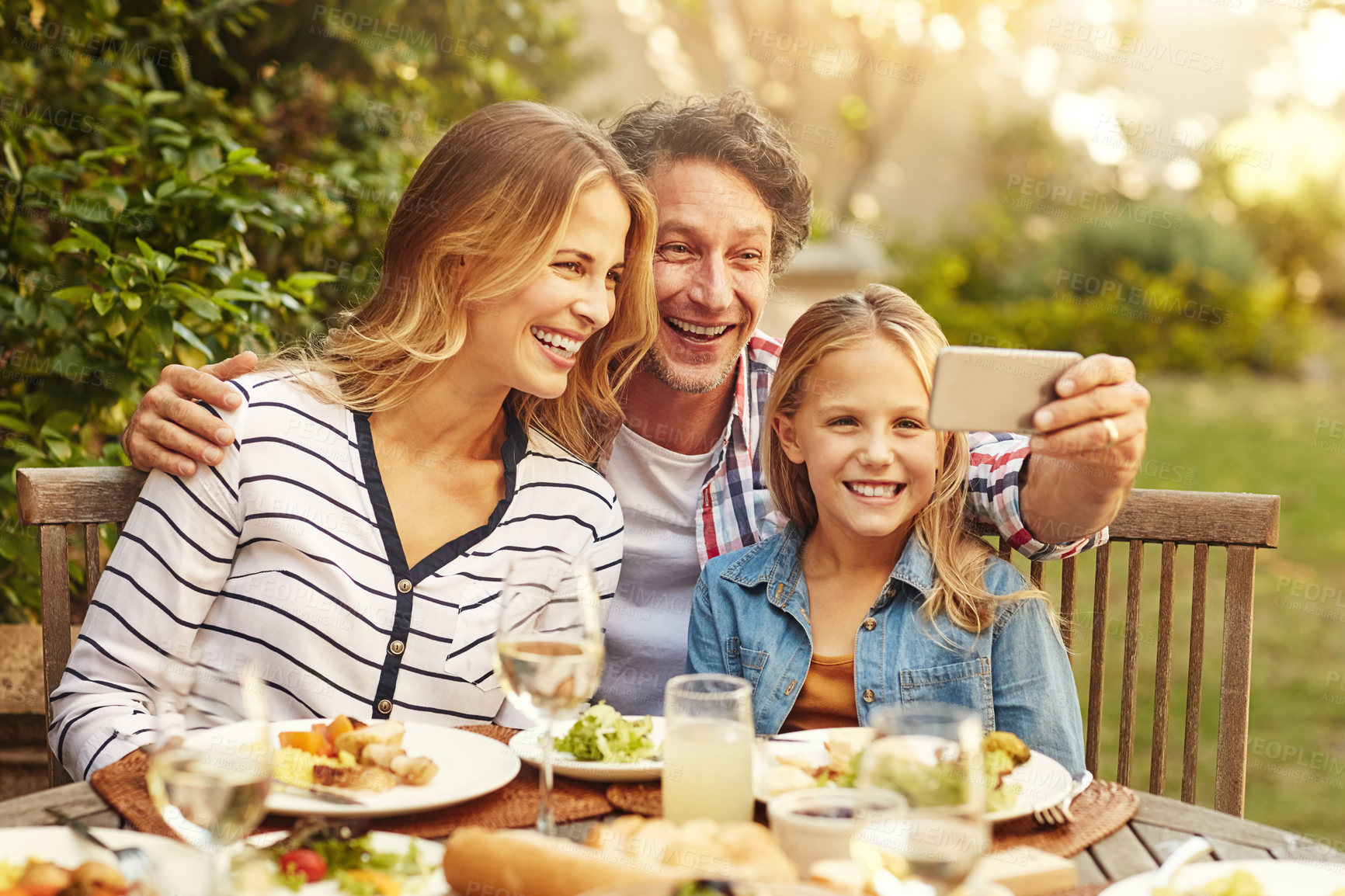 Buy stock photo Shot of a happy family taking a selfie together at an outdoor lunch