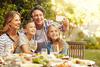 Buy stock photo Shot of a happy family taking a selfie together at an outdoor lunch