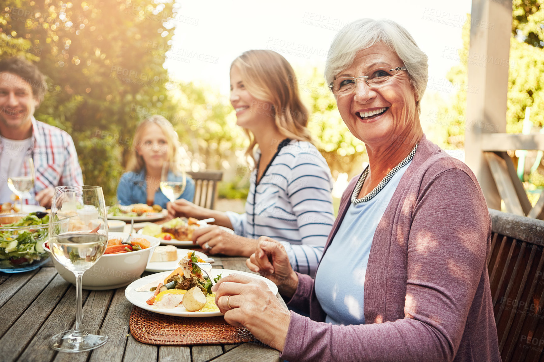 Buy stock photo Portrait of a happy elderly woman enjoying an outdoor lunch with her family
