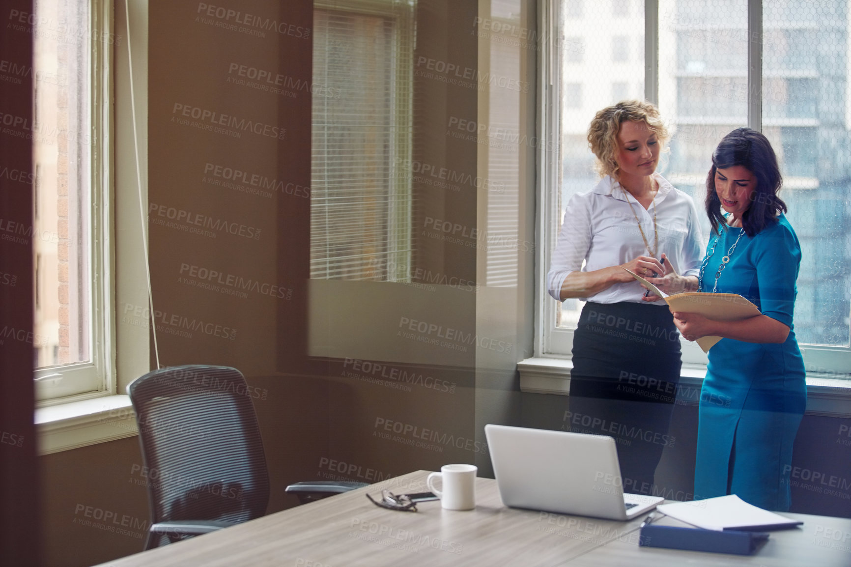 Buy stock photo Shot of two businesswomen going over paperwork together in an office