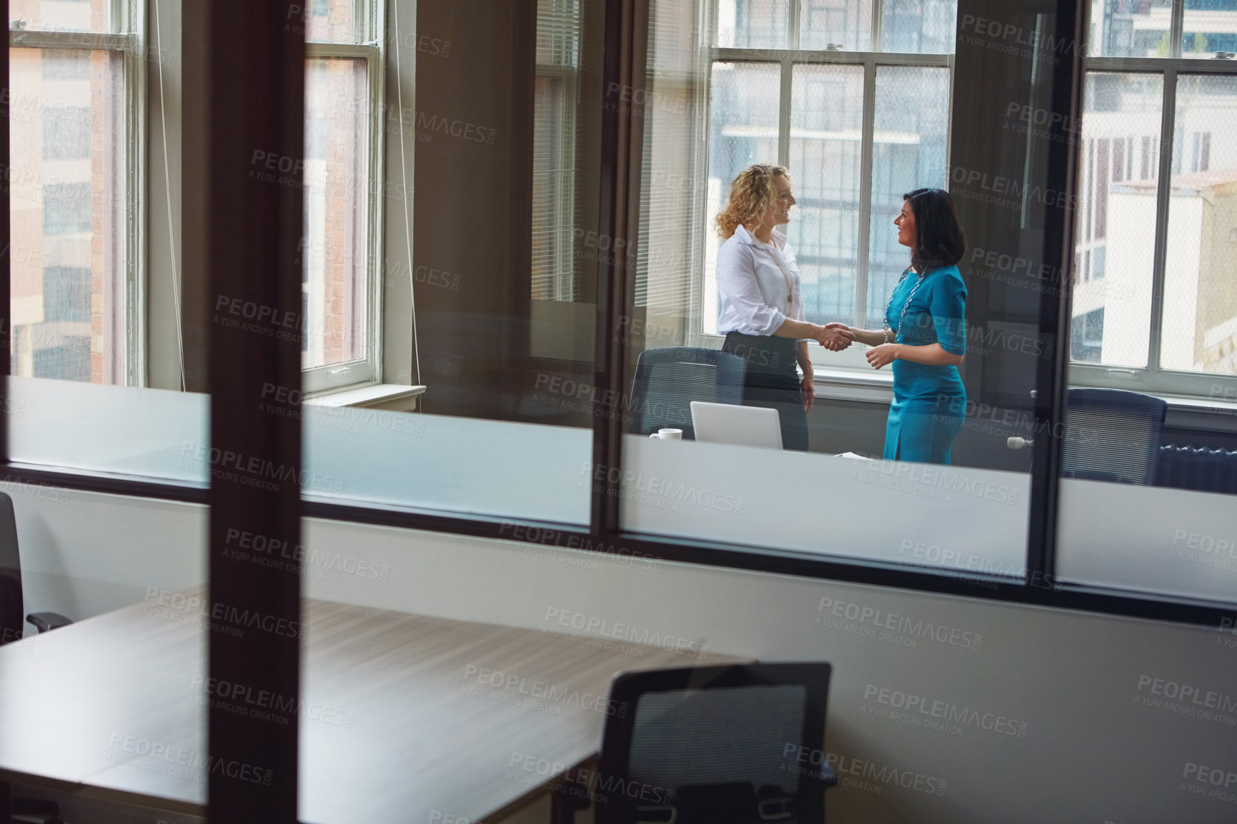 Buy stock photo Shot of two businesswomen shaking hands in an office