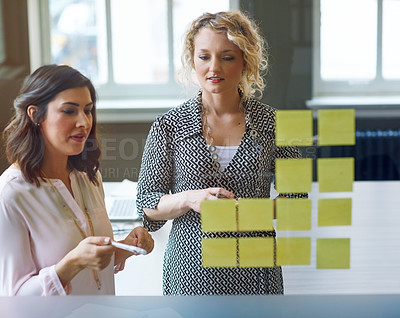 Buy stock photo Cropped shot of Shot of two businesswomen brainstorming with adhesive notes on a glass wall in an office working in the office
