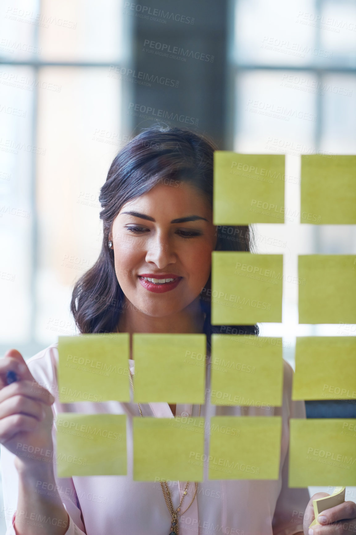 Buy stock photo Shot of a businesswoman brainstorming with adhesive notes on a glass wall in an office