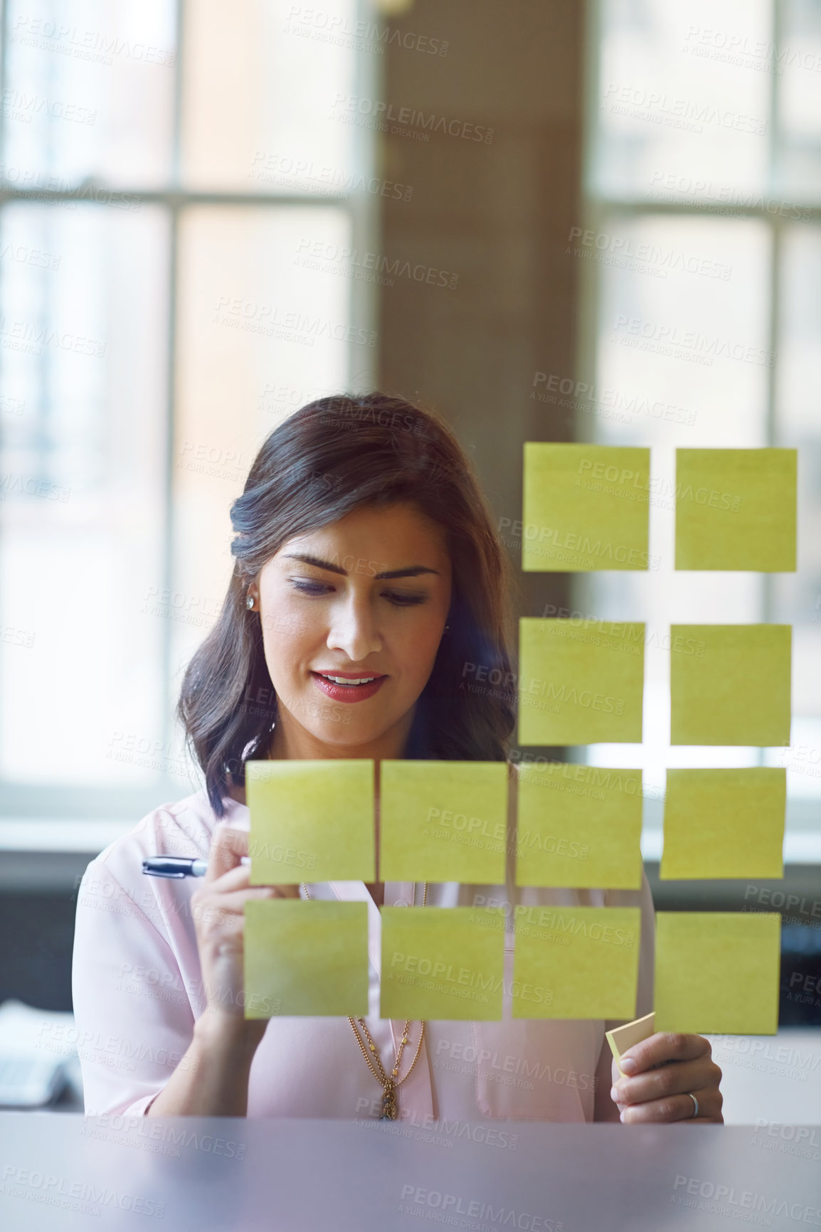 Buy stock photo Shot of a businesswoman brainstorming with adhesive notes on a glass wall in an office