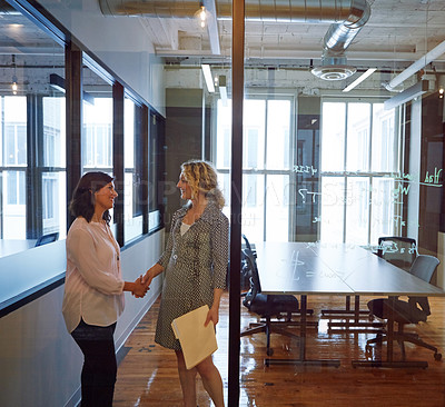Buy stock photo Shot of two smiling businesswomen shaking hands in an office