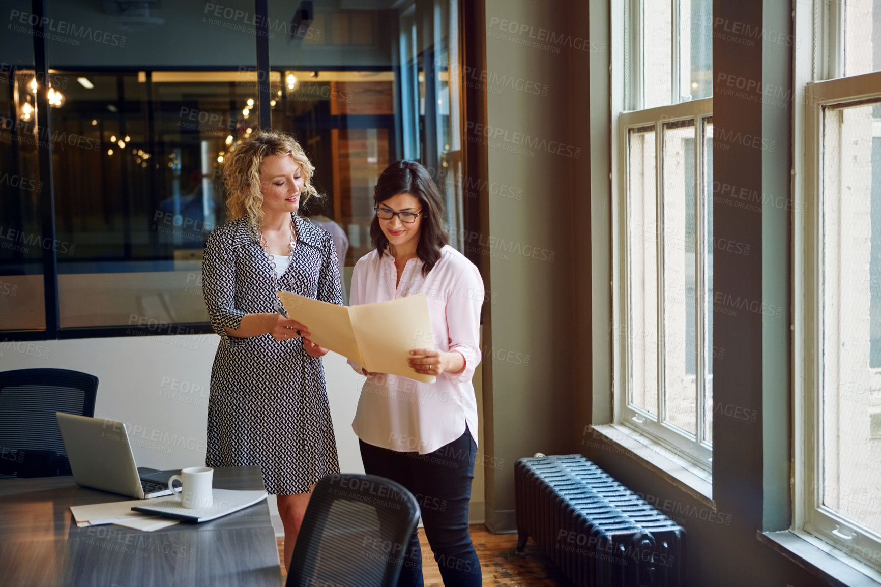 Buy stock photo Shot of two businesswomen talking together over paperwork in an office