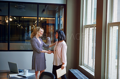 Buy stock photo Shot of two smiling businesswomen shaking hands in an office