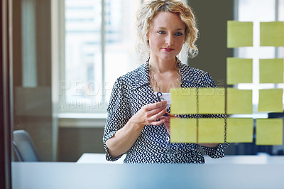 Buy stock photo Shot of a businesswoman brainstorming with adhesive notes on a glass wall in an office